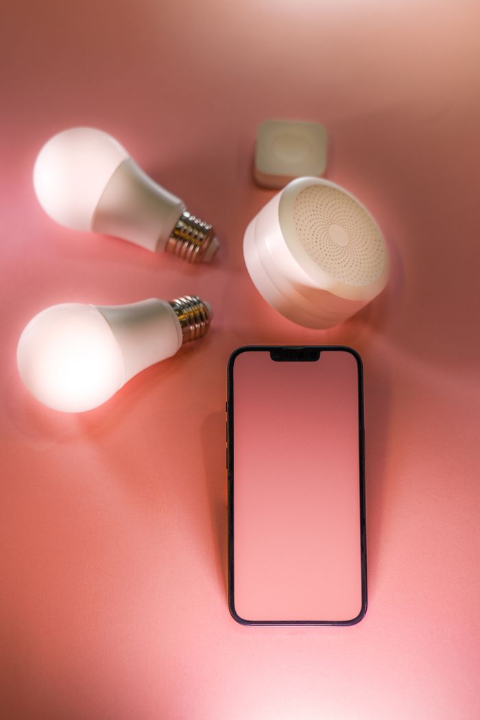 Stylish smartphone and smart bulbs flat lay on a pink background.
